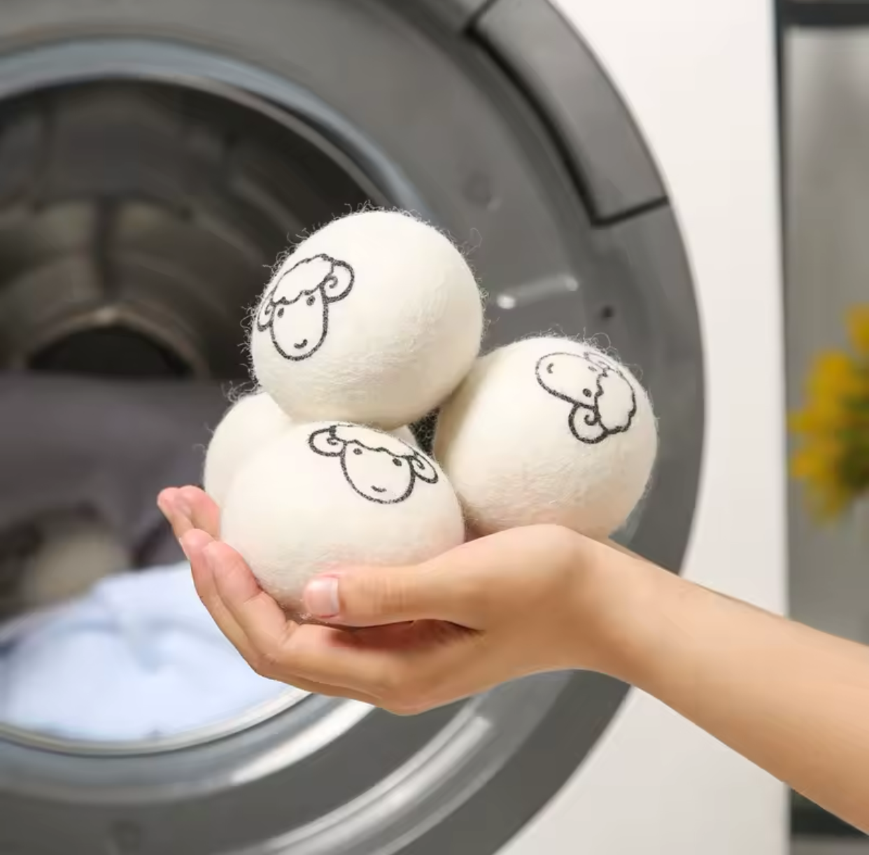 Balles de séchage en laine naturelle Flowza dans une main avec un sèche-linge en arrière-plan